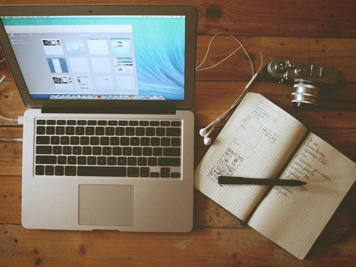 A laptop and sketchbook with wireframe notes on a wooden desk