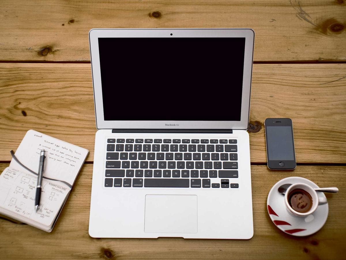 A laptop, notebook and coffee on a wooden desk